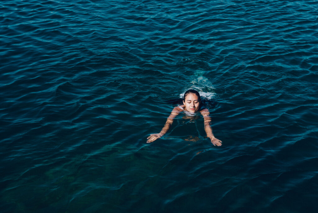 Young woman in white dress swim in the sea.