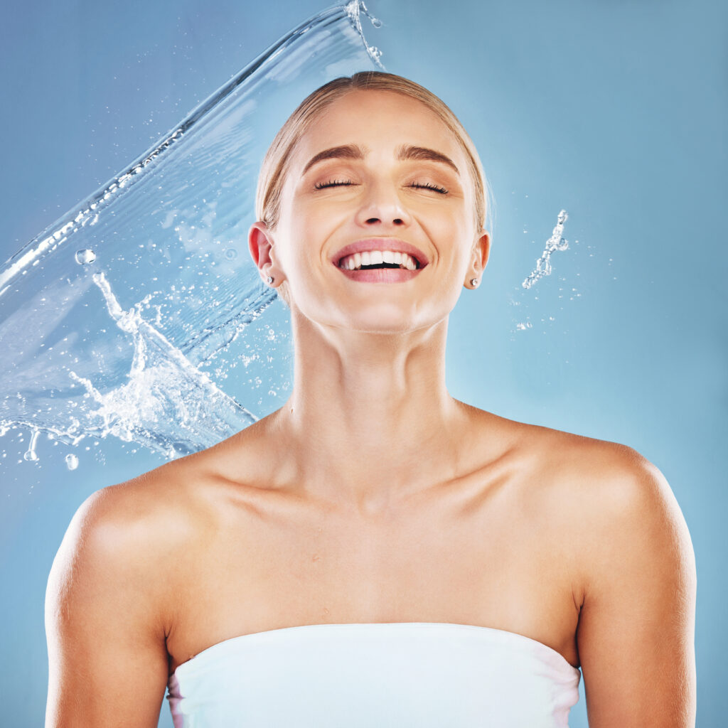 Water, beauty and cleaning with a model woman in studio on a blue background for hydration in a splash